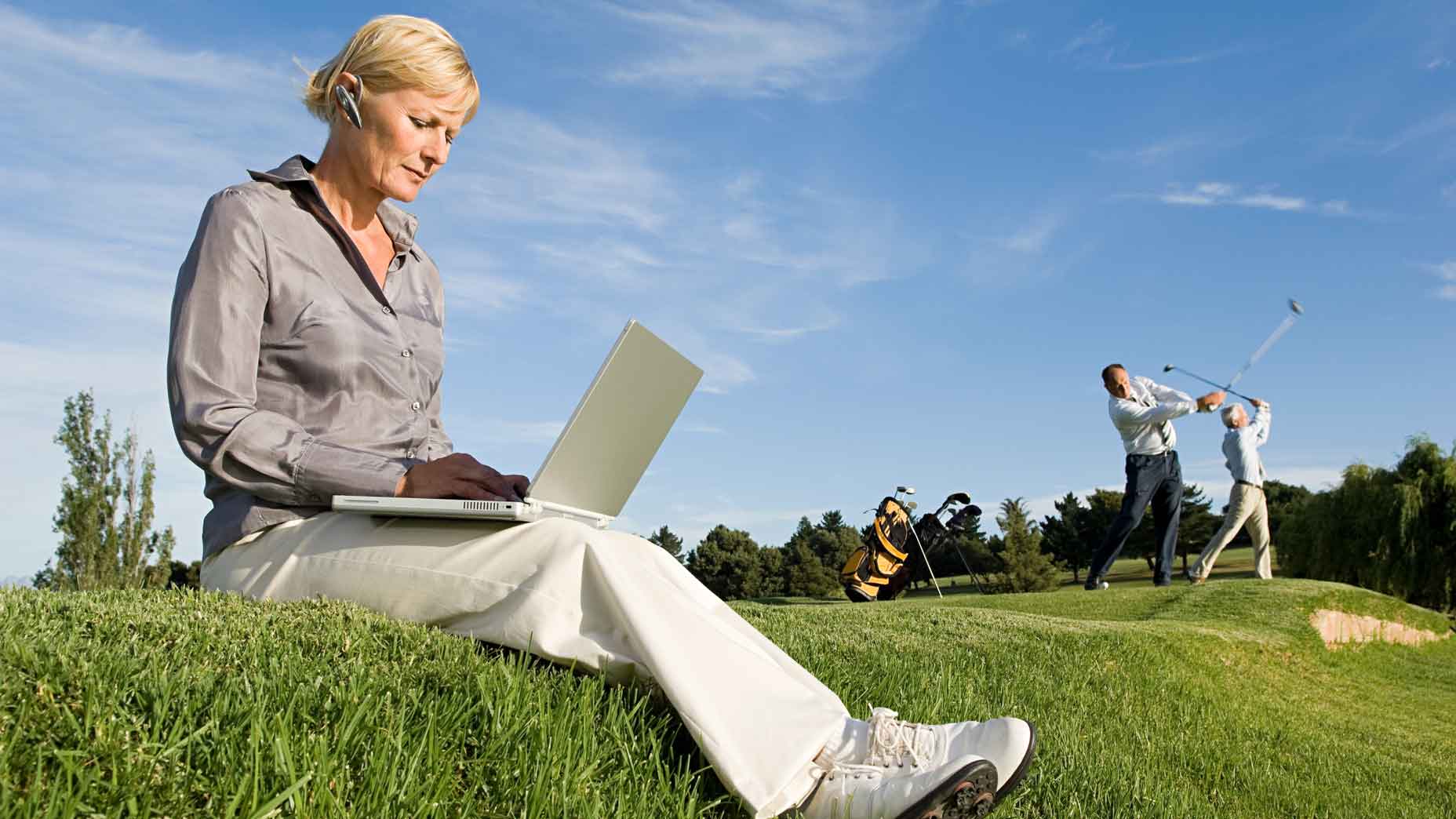 woman sits on laptop while golfers swing in background